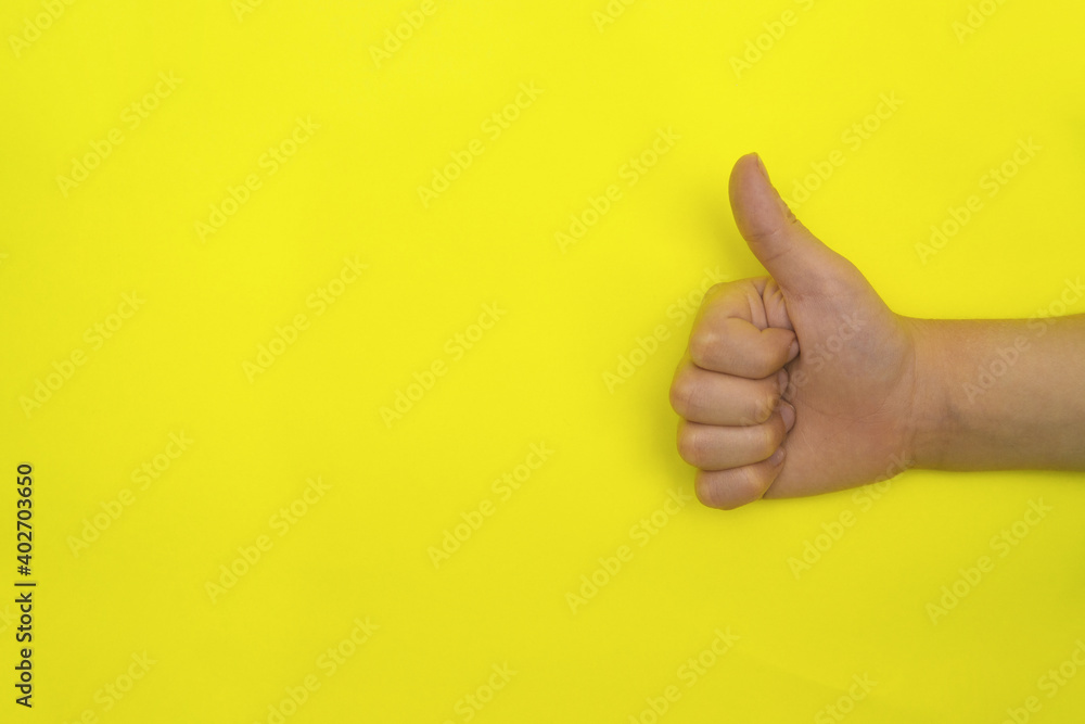 A child's hand shows a raised thumb on a yellow background.