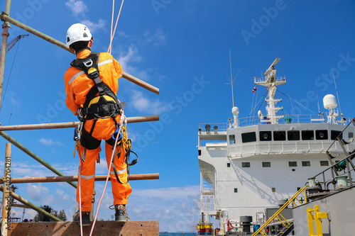 Worker abseiling from high places on the high scaffolding wear equipment protective safety harness on structure site project and shipyard on accommodation bridge deck of cargo ship background. © TawanSaklay