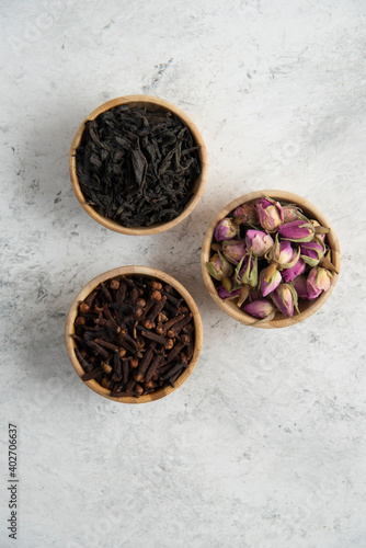 Three wooden bowls with dried roses, cloves and loose teas