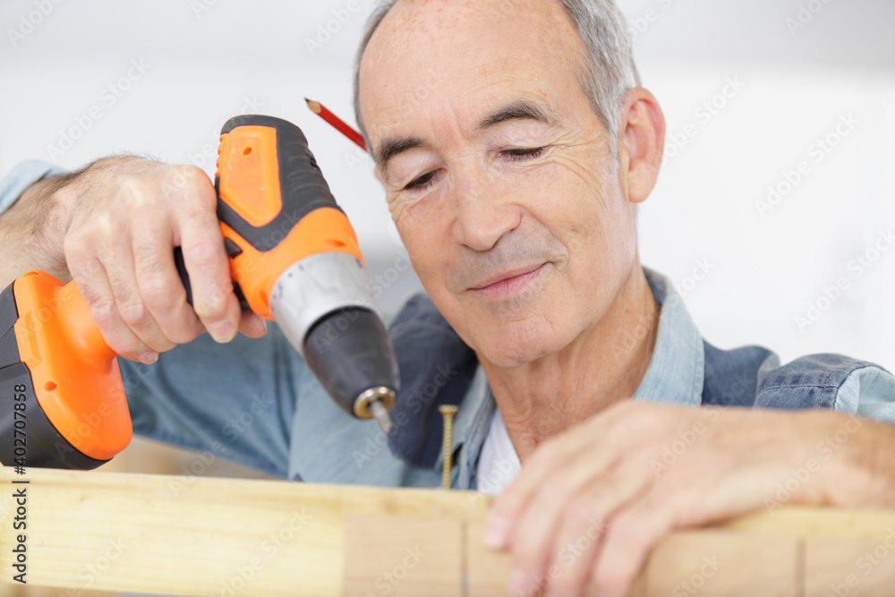 senior carpenter using cordless screwdriver on wood senior carpenter using cordless screwdriver on wood