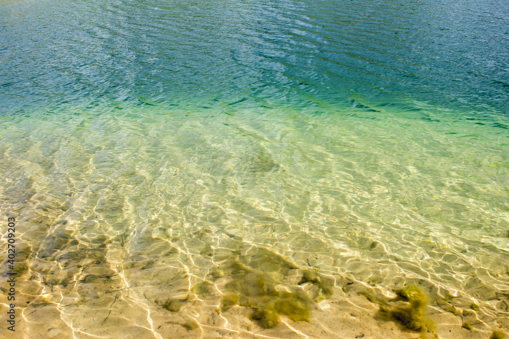Clear clear water of the lake with a turquoise hue on a sandy beach. The natural background Clear clear water of the lake with a turquoise hue on a sandy beach. The natural background