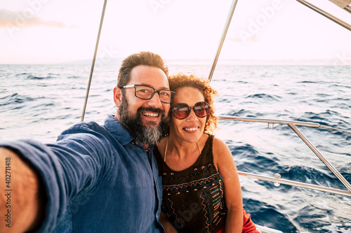 Cheerful people happy adult caucasian couple take selfie picture and enjoy together summer holiday vacation sailing boat with ocean and sky in background - tourists lifestyle and fun in outdoor ocean