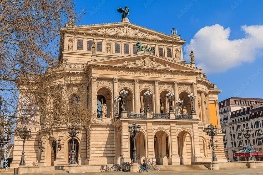 Square in the center of the city of Frankfurt. Buildings of the historic old opera house with trees and commercial buildings at springtime in sunshine. Bicycles in front of the steps