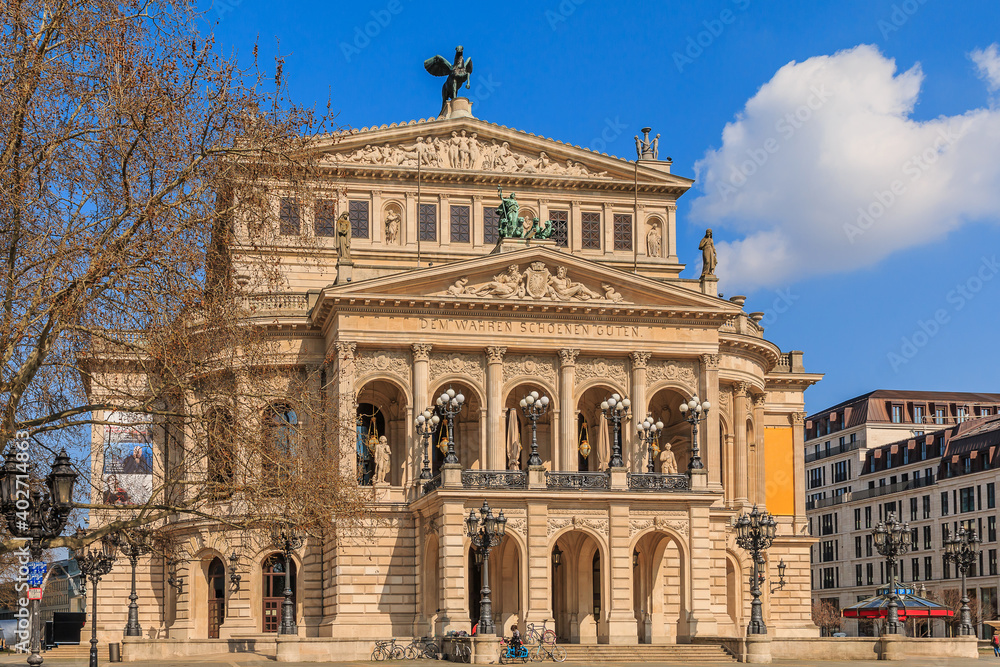 Buildings of the historic old opera house with trees and commercial buildings at springtime in sunshine with clouds in the sky. Square in the center of the city of Frankfurt.