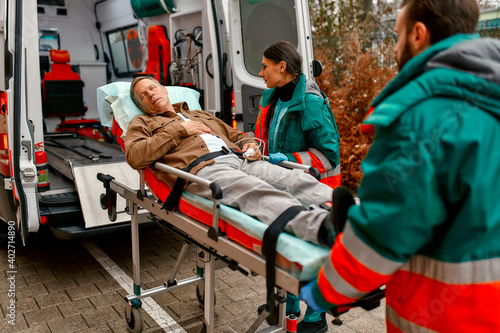 Paramedics take out a gurney with an elderly patient from a modern ambulance for further medical care at the clinic.