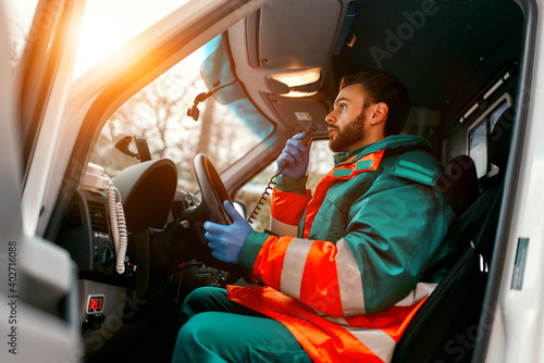An adult handsome male paramedic is talking on a portable radio while sitting in an ambulance outside a clinic. photo