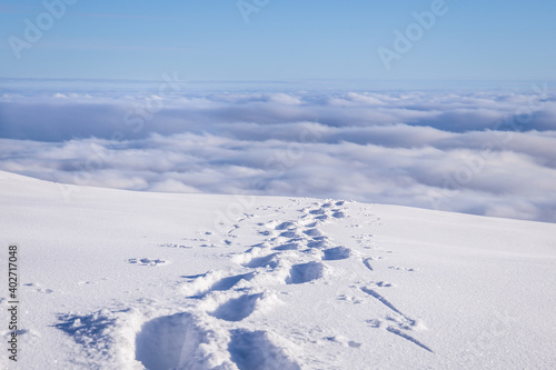 Foot steps through deep snow above the fog in a beautiful winter landscape 