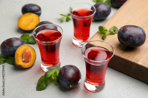 Delicious plum liquor, mint and ripe fruits on light table. Homemade strong alcoholic beverage