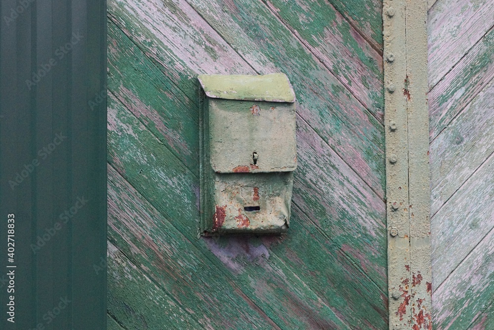 one old green metal mailbox hanging on a  wooden fence in the street
