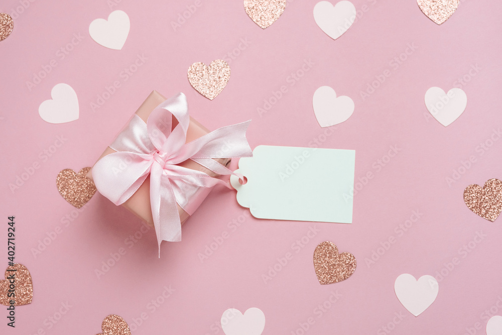 Gift box with blank gift tag on pastel pink background with many hearts. Valentines day composition. Top view, flat lay.