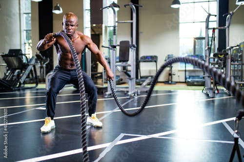 young african muscular athlete working out with ropes in gym