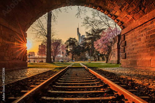 Old tunnel with track in the evening at sunset in Frankfurt am Main bank. Park with trees and flowers. High-rise buildings from the financial district in the city center