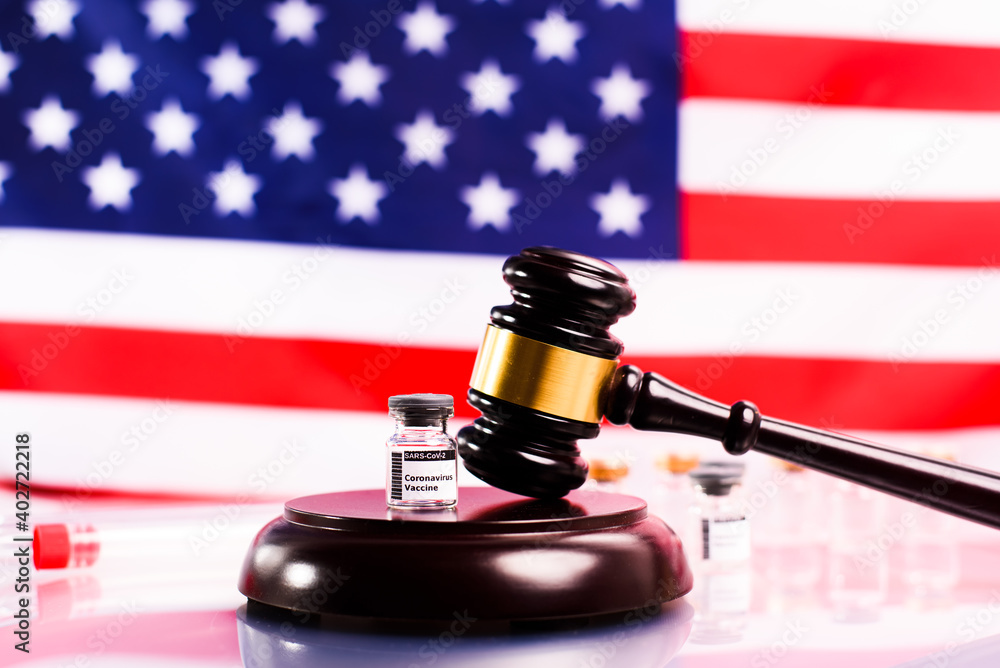 Judicial gavel on the pharmacies that sell coronavirus vaccine, with an unfocused American flag background.
