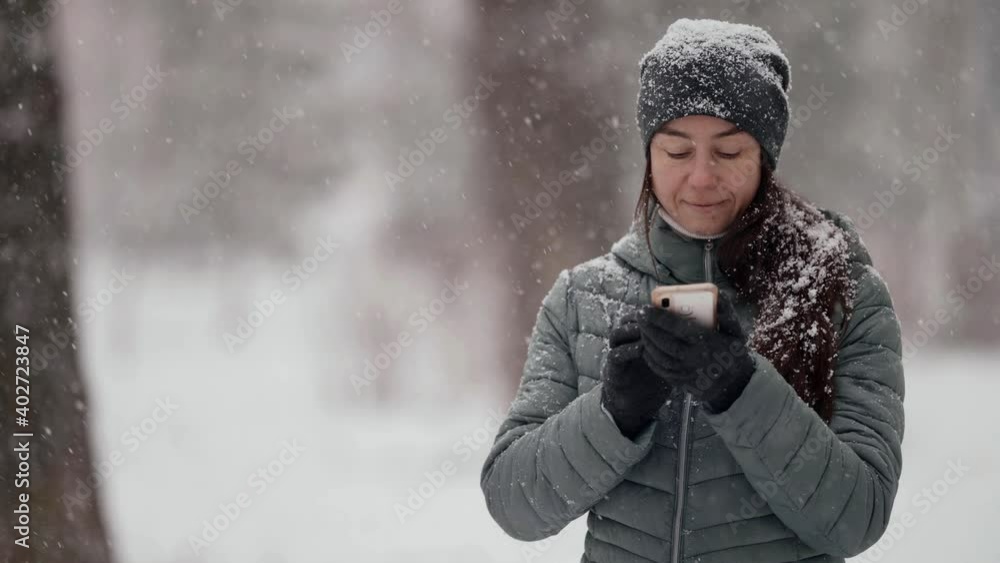 adult woman is using smartphone outdoors, reading messages at winter snowy day on street adult woman is using smartphone outdoors, reading messages at winter snowy day on street