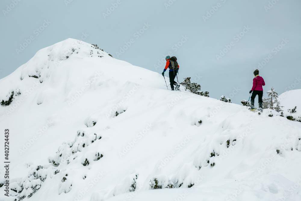 Two hikers alpinist climbing up the snowy mountain on Sunset. Alpine winter view. Carpathians, Marmarosy