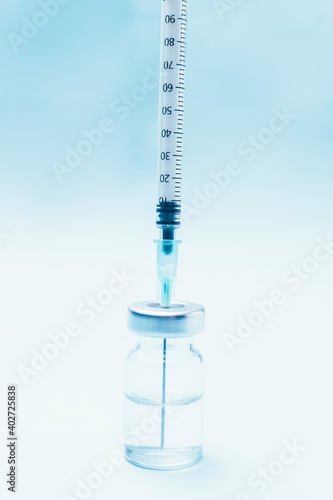 Punctured syringe in a bottle to put a vaccine on blue background.