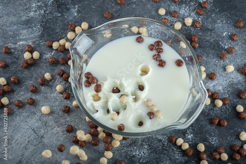 Bowl of milk with splashing cereal balls on marble background