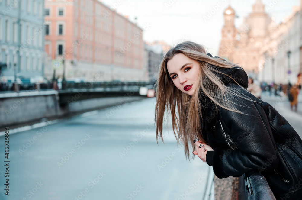 Fototapeta premium Portrait of a young blonde woman in black clothes on the bank of the canal in St. Petersburg
