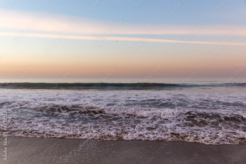 Waves washing ashore in colorful sunrise at Malibu Beach, California