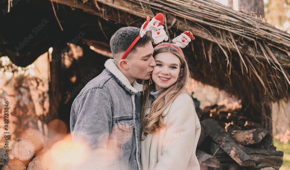 A couple dressed in New Year's hoops on their heads are smiling at each other against the background of a gazebo made of firewood