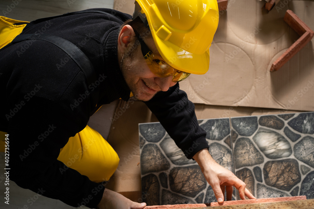 The builder applies brick-shaped decorative tiles to the furniture board and checks if they fit exactly. Construction worker wearing personal protective equipment. The builder applies brick-shaped decorative tiles to the furniture board and checks if they fit exactly. Construction worker wearing personal protective equipment.