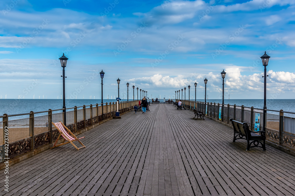 A view along Skegness pier, UK with a modern wind farm just visible on the horizon on a bright autumn afternoon