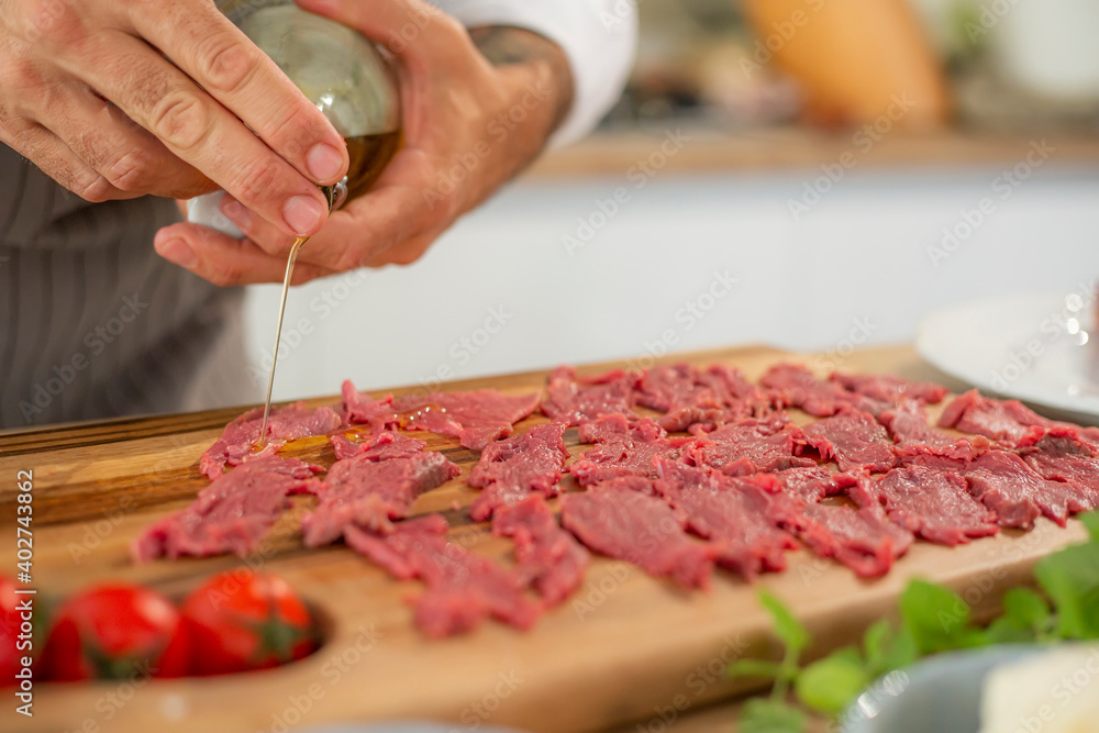 A close-up of the chef's hands adding olive oil to the carpaccio meat