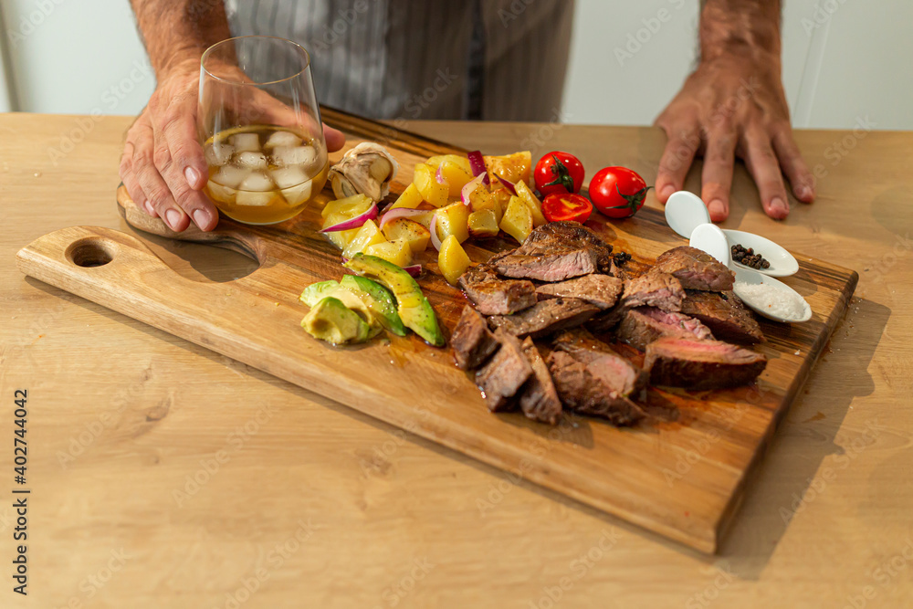 Close-up of roasted meat on a wooden board with whiskey in background