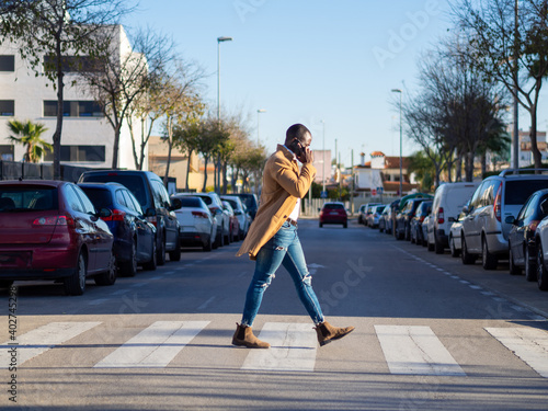 Hombre negro cruzando la calle mientras habla con el teléfono móvil