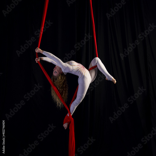 beautiful aerialist on red aerialsilks balances in split, strong graceful girl