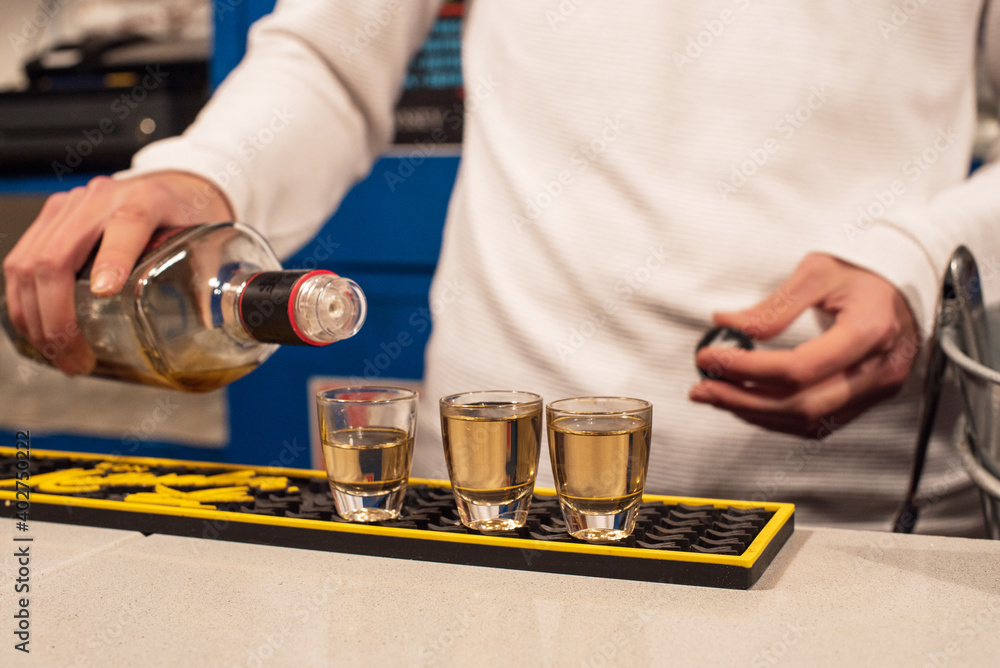 Un camarero joven llena unos vasos de chupito de una bebida alcohólica de color marrón en la barra de un bar Un camarero joven llena unos vasos de chupito de una bebida alcohólica de color marrón en la barra de un bar