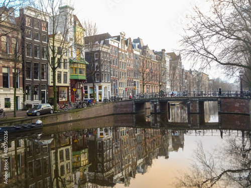 Amsterdam canal with beautiful historical houses and bridge with reflection in the water during winter, Amsterdam, Netherlands