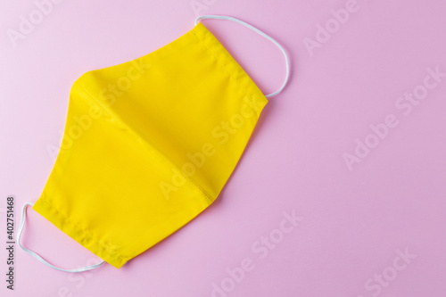 Reusable protective mask made from yellow cotton. Yellow face mask on a pink background. Face protective mask. Pop art style. Flat lay. Copy space
