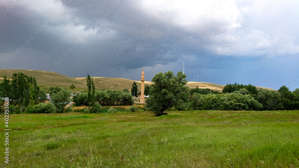 Distant and pastoral view of a village in Anatolia, Turkey with clouds in the sky, tress and mosque.
