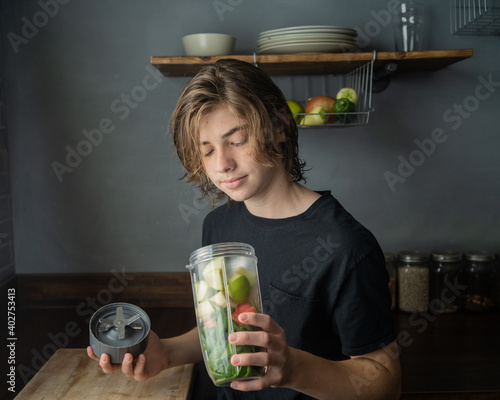 teen boy looking at smoothie with vegetables and fruit and smiling