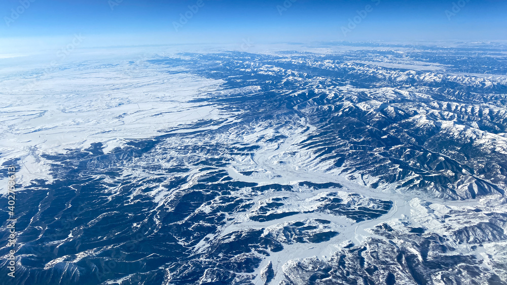 An aerial view from an airplane window of mountains, snow, clouds and blue skies.