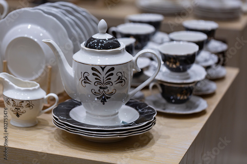 Fototapeta Naklejka Na Ścianę i Meble -  Creative shot of tea pot and White crockery for tea in shallow depth of field. Cups and saucers on a wooden table. Set cups and teapot in restaurant for event celebration.