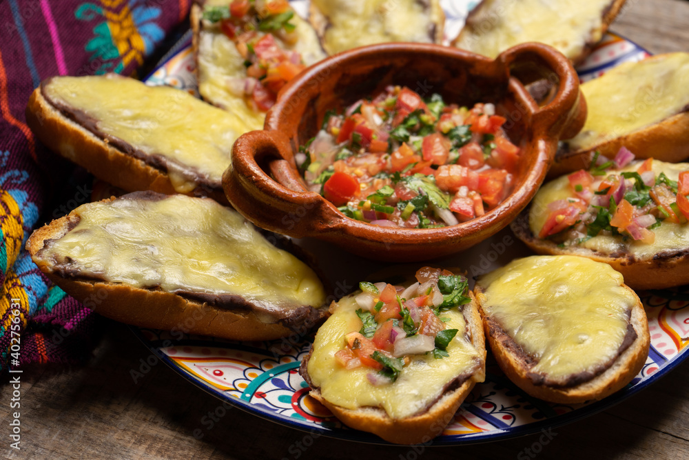 Mexican molletes with cheese and fresh sauce on wooden background Mexican molletes with cheese and fresh sauce on wooden background