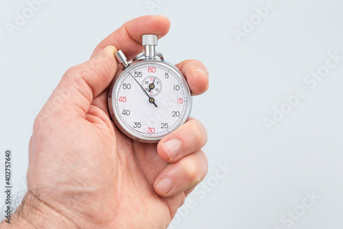 Man holding analog stopwatch on the gray background.