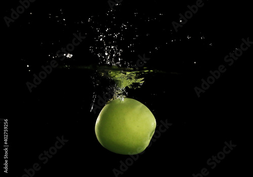 Green apple falling down into clear water against black background