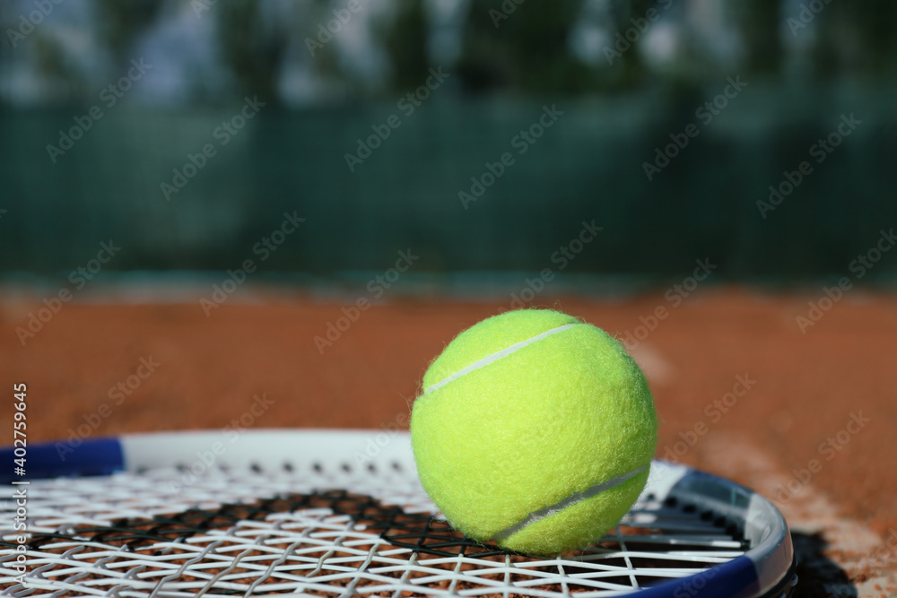 Tennis ball and racket on clay court, closeup. Space for text