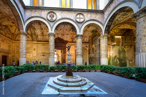 The first courtyard of the Palazzo Vecchio in Florence Italy with a small fountain with statue, frescoes on the wall and vaulted columns.