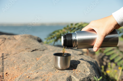 Woman pouring hot drink from thermos into cap outdoors, closeup photo