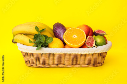 Assortment of fresh exotic fruits in basket on yellow background