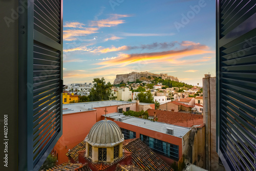 Sunset view of the ancient Parthenon and Acropolis Hill through an open window overlooking the Plaka district of Athens, Greece.