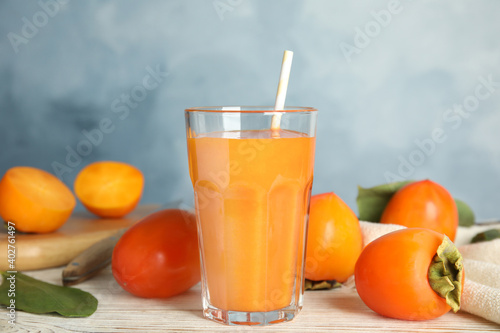 Fresh tasty persimmon smoothie and fresh fruits on white wooden table against light blue background