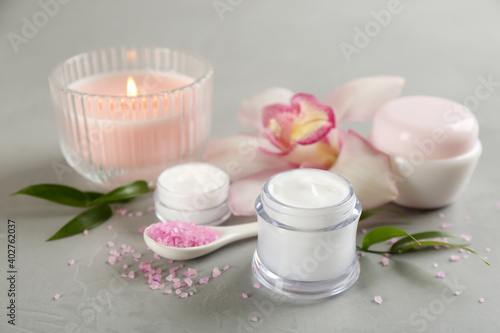 Beautiful spa composition with cosmetic products, flowers and candle on light grey table