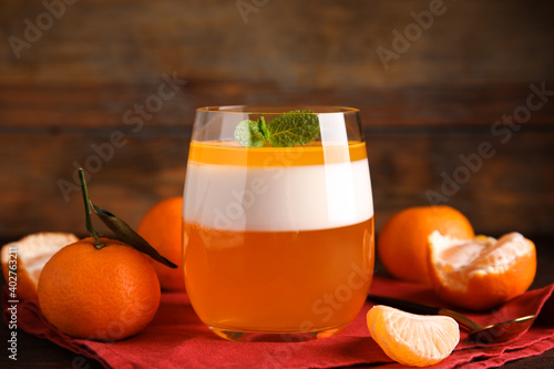 Delicious tangerine jelly in glass and fresh fruits on table, closeup