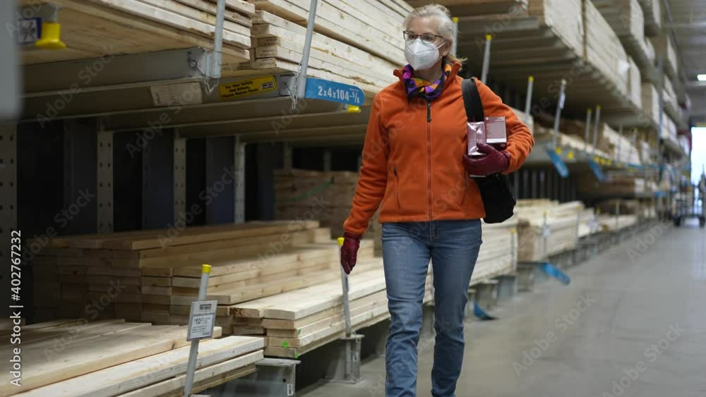 Mature woman wearing face mask walking through the lumber section of a big box hardware store. Mature woman wearing face mask walking through the lumber section of a big box hardware store.