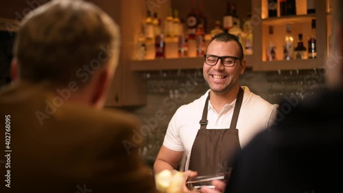 a smiling and sociable bartender conducts a conversation with customers in the bar. Evening in the restaurant, communication of bar guests with the bartender photo